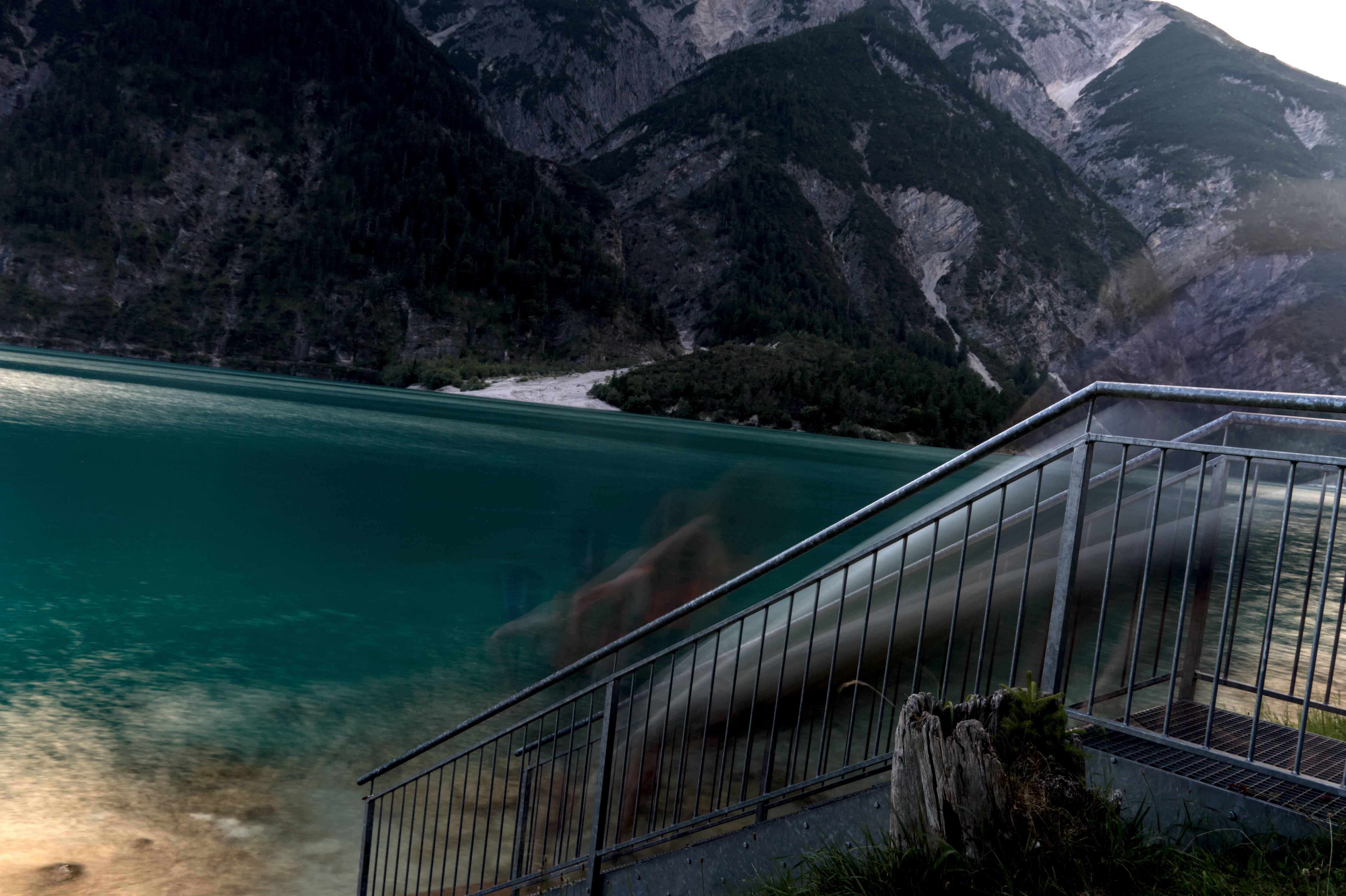 A long exposure image, of a blurred paddleboard being carried by blurry people up stairs, with blurred water behind