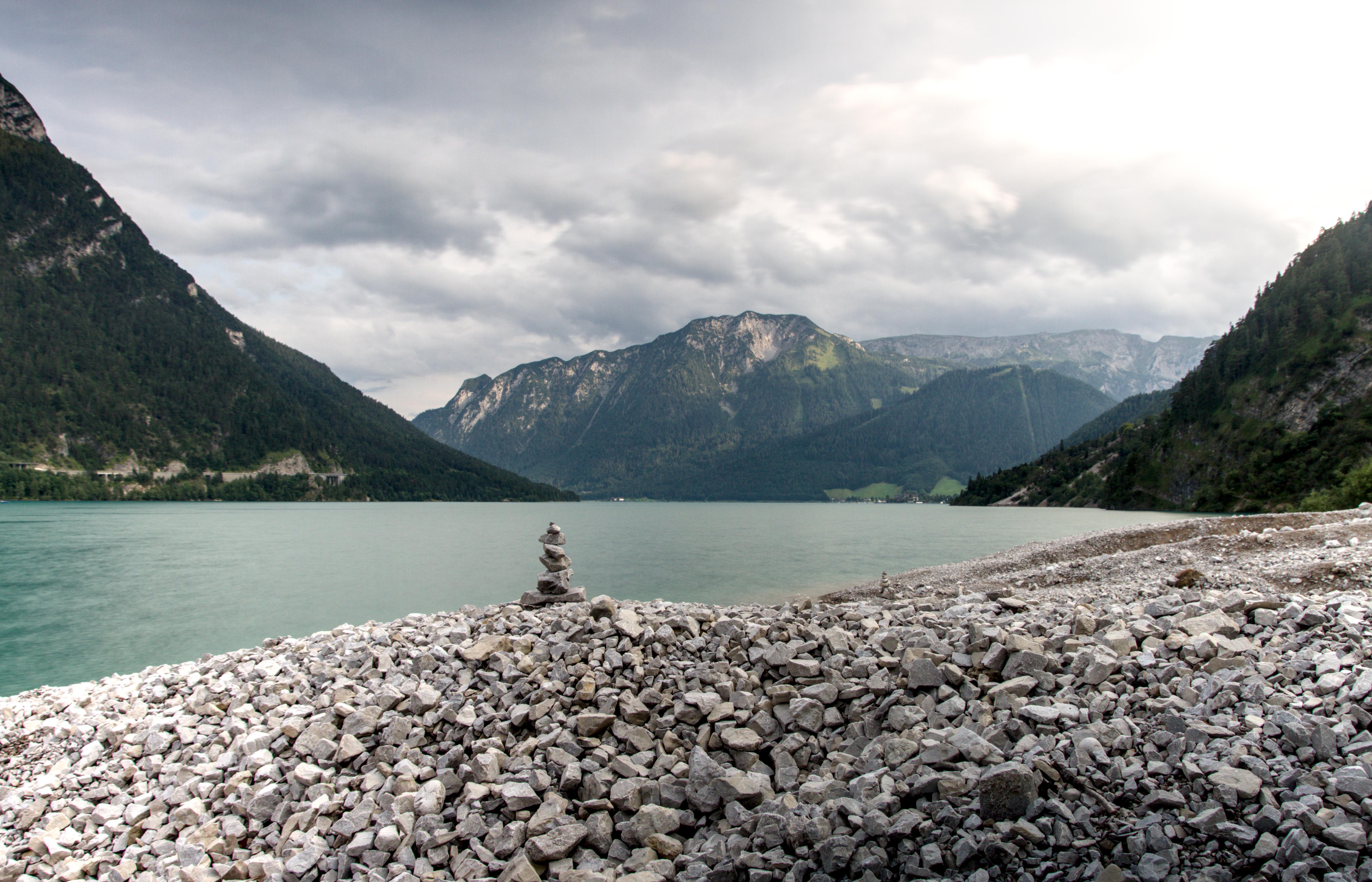 A stack of rocks on top of a lot of scree. The water is blurred from long exposure, with massive mountains behind.