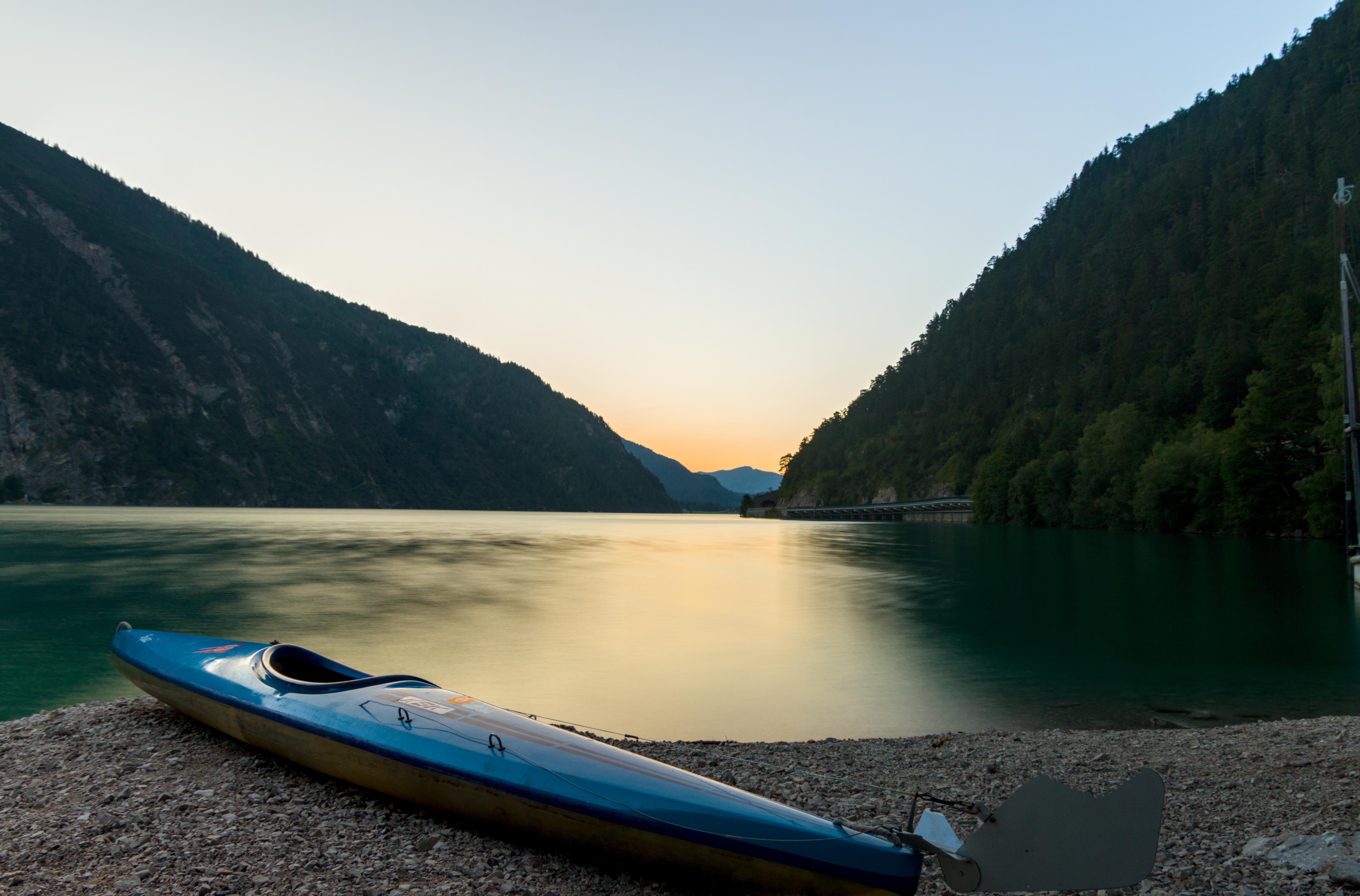 A kayak on scree, overlooking a glassy and blurred lake, with mountains in the distance.